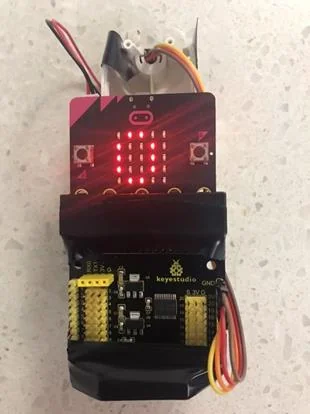 CovidEye prototype: a BBC micro:bit showing a red LED pattern, mounted on a sensor expansion board with an infrared temperature sensor
